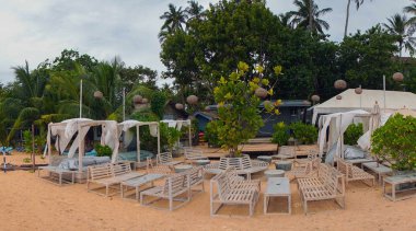 Beyaz masa ve koltukları plajda palmiye ağaçları altında.