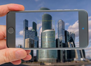 Modern şehirde cam gökdelenler. Bir adamın elindeki akıllı telefon. 