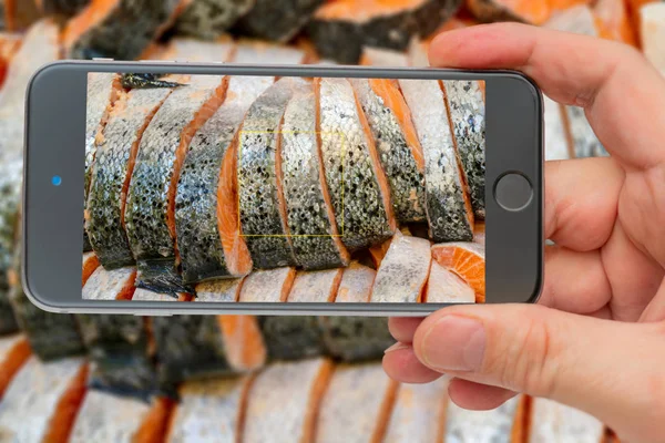 Salmon steak on counter ice in supermarket. Photo smartphone. Smartphone in hand. Salmon on screen.