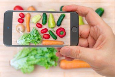 Sebzeler akıllı telefon ekranında. Tahta kesme tahtasında taze sebzeler. Sağlıklı yemek pişirmek için sebze seti..