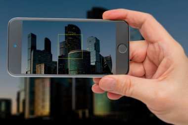 Akıllı telefon ekranındaki binalar. Gün batımında gökdelenler. Gece şehrin ışıkları.