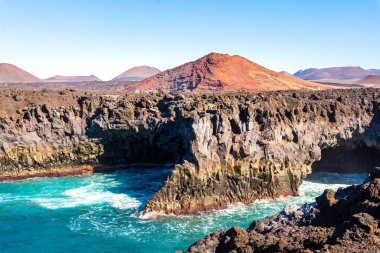  Los Hervideros, Lanzarote, Kanarya Adaları, İspanya. Okyanustaki lav kayalıkları, arka plandaki volkanlar.