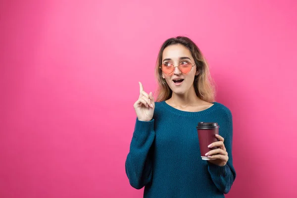 ピンクの背景にコーヒーを飲みながら青いセーターを着たグラマーな女性 — ストック写真