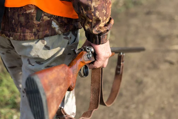 A man with a gun in his hands and an orange vest on a pheasant hunt in a wooded area in cloudy weather. Hunter with dogs in search of game.