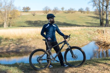 Pantolon ve yün ceketli bisikletçi modern karbon donanımlı bir motorsikletle off-road 'a biniyor..