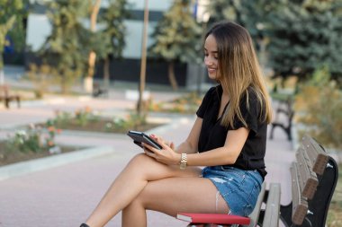 Genç bir kız parkta bir bankta oturur ve notlar yapar. Serbest stilde giyinmiş. Müşterilerle telefonda konuşan iş kadını.