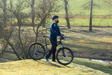 Pantolon ve yün ceketli bir bisikletçi. Havalandırma çatallı, modern bir karbon motorlu. Tepedeki adam bisiklete biniyor..