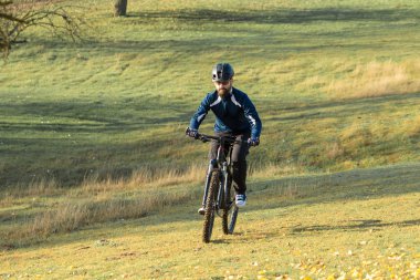 Pantolon ve yün ceketli bir bisikletçi. Havalandırma çatallı, modern bir karbon motorlu. Tepedeki adam bisiklete biniyor..