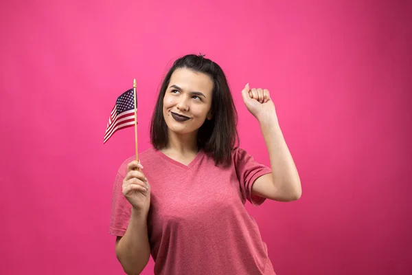 快乐的年轻女子拿着美国国旗面对着粉红的工作室背景 — 图库照片