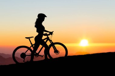 Dağ bisikletli bir kız, gün batımında bir bisikletçinin güzel portresi spor kıyafetleriyle modern bir karbon fiber dağ bisikleti, bir kask, gözlük ve eldiven sürüyor.