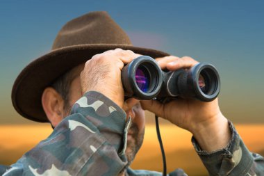 Kamuflajlı bir avcı ve sabahın erken saatlerinde elinde bir silah bir dağın tepesinde bir hedef arıyor. Güzel dağ manzarası, avın açılışı..