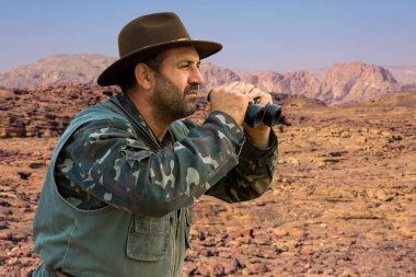 Kamuflajlı bir avcı ve sabahın erken saatlerinde elinde bir silah bir dağın tepesinde bir hedef arıyor. Güzel dağ manzarası, avın açılışı..