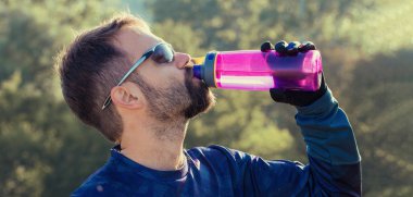 Gözlüklü atletik genç adam şişeden su içiyor. Tonlanmış panoramik resim.