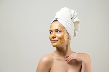 Yüzünde altın besleyici maske olan beyaz havluyla kadın portresi. Cilt temizleme eko organik kozmetik rahatlama konsepti.