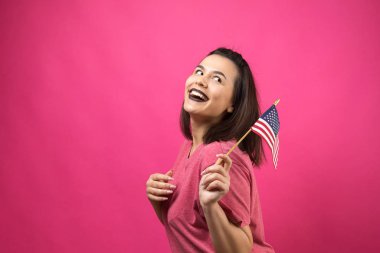 Stüdyonun pembe arka planında Amerikan bayrağı tutan mutlu genç kadın.