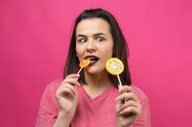 Güzel, güzel, neşeli, düz kahverengi saçlı bir kadının portresi. Gözlerinin yanında lolipop tutuyor..