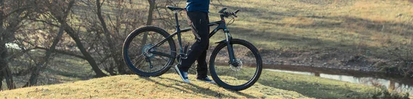 エアサスフォーク付きのモダンなカーボンハードテールバイクのパンツとフリースジャケットでサイクリスト 丘の上の男は自転車に乗っている — ストック写真