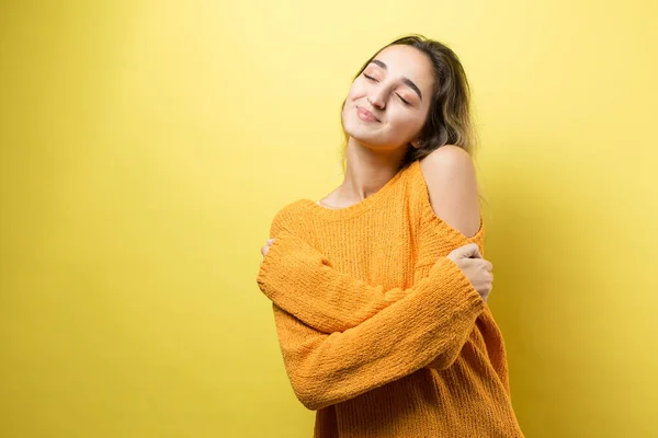 Happy young beautiful caucasian woman hugging herself on yellow background