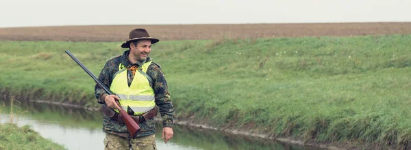 Hunting period, autumn season open. A hunter with a gun in his hands in hunting clothes in the autumn forest in search of a trophy. A man stands with weapons and hunting dogs tracking down the game.