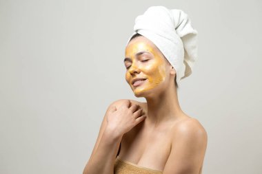 Yüzünde altın besleyici maske olan beyaz havluyla kadın portresi. Cilt temizleme eko organik kozmetik rahatlama konsepti.