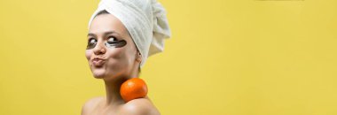Yüzünde altın besleyici maske olan beyaz havluyla kadın portresi. Cilt temizleme organik kozmetik rahatlama konsepti. Sırtı turuncu bir mandalina tutan bir kız..