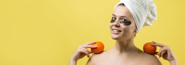 Yüzünde altın besleyici maske olan beyaz havluyla kadın portresi. Cilt temizleme organik kozmetik rahatlama konsepti. Sırtı turuncu bir mandalina tutan bir kız..