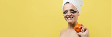 Yüzünde altın besleyici maske olan beyaz havluyla kadın portresi. Cilt temizleme organik kozmetik rahatlama konsepti. Sırtı turuncu bir mandalina tutan bir kız..