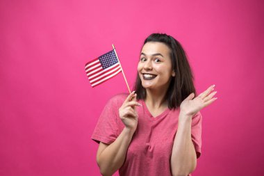 Stüdyonun pembe arka planında Amerikan bayrağı tutan mutlu genç kadın.