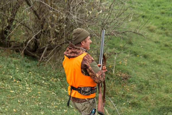狩猎期 秋季开放 一个拿着猎枪的猎人穿着猎服在秋天的森林里寻找奖品 一个人拿着武器和猎狗站在那里追踪猎物 — 图库照片