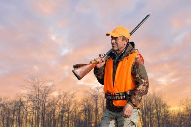 Kızıl şafağın arka planında bir avcının silueti. Elinde silahla hazır bekliyor..