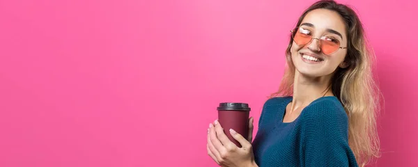 ピンクの背景にコーヒーを飲みながら青いセーターを着たグラマーな女性 — ストック写真