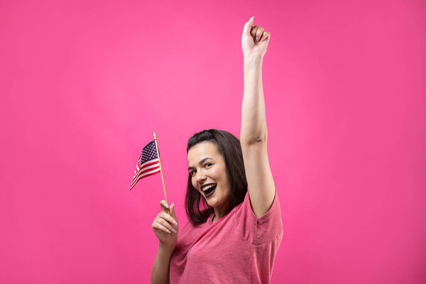 Happy young woman holding American flag against a studio pink background