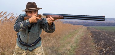 Avcı, elinde silahla sonbahar ormanında av elbisesi içinde ganimet arıyor. Bir adam silahla ayakta durur..