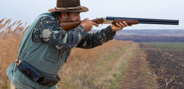Avcı, elinde silahla sonbahar ormanında av elbisesi içinde ganimet arıyor. Bir adam silahla ayakta durur..
