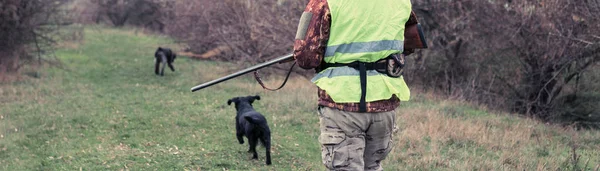 狩猟期間 秋のシーズンを開いています 秋の森の中でトロフィーを求めて狩猟服を手に銃を持ったハンター 男は武器と狩猟犬と一緒に立ってゲームを追跡する — ストック写真