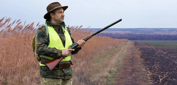 一个拿着猎枪的猎人穿着猎服在秋天的森林里寻找奖品 一个男人拿着武器站在那里 — 图库照片