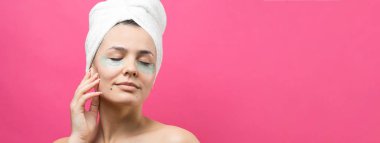 Kafasında beyaz havluyla gezen genç bir kız gözlerinin altına kolajen jel bantlar takıyor. Göz teması altında maske.