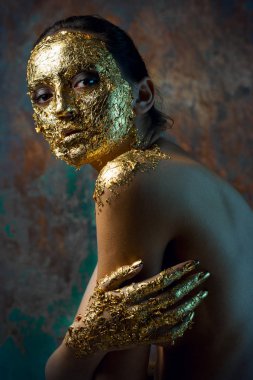 Yüzünde altın yapraktan yapılmış bir maske olan bir kız. Soyut bir arka planda esmer bir kadının kasvetli stüdyo portresi.
