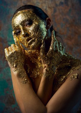 Yüzünde altın yapraktan yapılmış bir maske olan bir kız. Soyut bir arka planda esmer bir kadının kasvetli stüdyo portresi.