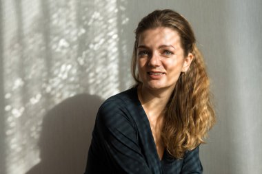 Arka planda, gölgeli gri bir duvarın üzerinde, penceresinden yansıyan doğal ışık olan güzel bir kızın portresi..