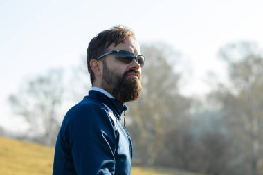 Pantolon ve yün ceketli bir bisikletçi modern karbon donanımlı bir motorsikletle off-road 'a biniyor. Adam parkta bir kütüğün üzerinde dinleniyor, uzaklığa bakıyor..