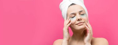 Kafasında beyaz havluyla gezen genç bir kız gözlerinin altına kolajen jel bantlar takıyor. Göz teması altında maske.