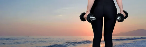 一位身穿运动服的苗条身材的年轻女运动员在海边做了一系列的运动 以抵御日落 用哑铃进行练习 健康和健康的生活方式 — 图库照片