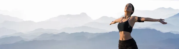 A thin athletic girl takes a break between classes on the background of mountains in the early morning, enjoys silence and freedom.