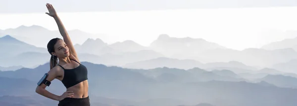 A thin athletic girl takes a break between classes on the background of mountains in the early morning, enjoys silence and freedom.