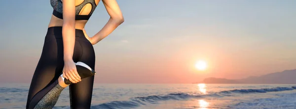 A thin athletic girl takes a break between classes on the background of the sunset by the sea in the early morning, enjoys silence and freedom.