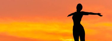 Spor giyimli genç, zayıf, atletik bir kız bir takım egzersizler yapıyor. Fitness ve sağlıklı yaşam tarzı. Gün batımında siluet.