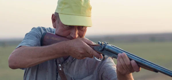 A man with a gun in his hands and an green vest  on a pheasant hunt in a wooded area in cloudy weather. Hunter with dogs in search of game.