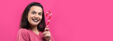 Güzel, güzel, neşeli, düz kahverengi saçlı bir kadının portresi. Kırmızı şeker kamışı Noel 'ini ısırmaya çalışıyor..