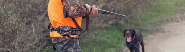 在多云的天气里 一个拿着枪 穿着橙色背心在森林里猎杀野鸡的男人 带着狗寻找猎物的猎人 — 图库照片